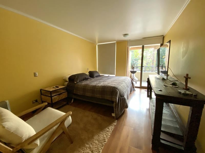 Dormitorio principal con cama de dos plazas, salida a terraza propia y muro en tono cálido.