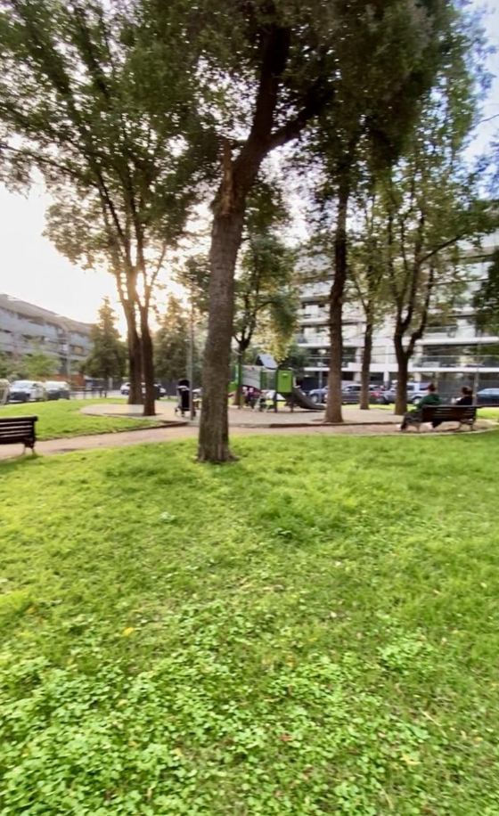 Plaza arbolada del barrio con juegos infantiles y bancas.