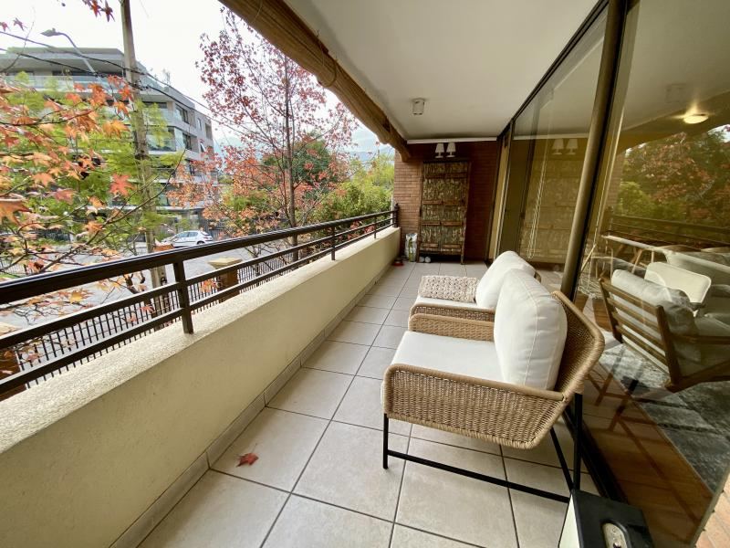 Terraza con sillones de mimbre y vista al follaje rojo de los árboles del parque en otoño.